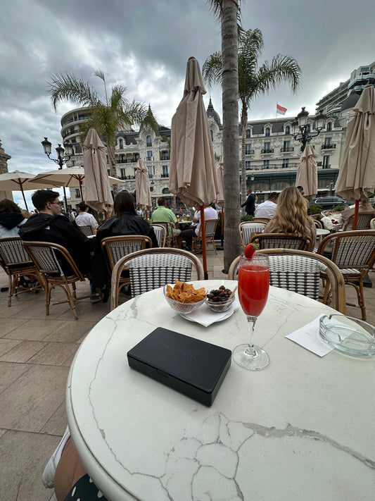 Travel adapters, make up beauty vanity travel cosmetics case, passport, power bank, city view of monaco cafe de monaco cocktail in europe summer.